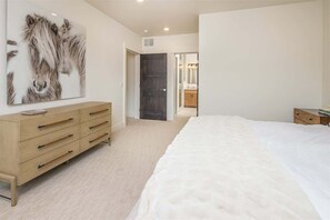 A bedroom with a large bed, a wooden dresser, and a painting of horses on the wall.
