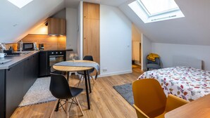A compact, modern apartment with a kitchen, dining area, and sleeping space. It features skylights, wooden flooring, and a bed with a leaf-patterned duvet. - Studio C, in the center of town, cosy and warm. (La Roche-sur-Yon)