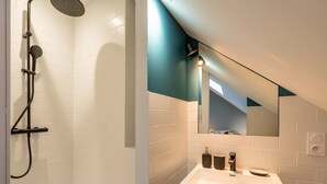 A modern bathroom with white tiles, a shower, a sink with a mirror, and a teal accent wall. - Studio C, in the center of town, cosy and warm. (La Roche-sur-Yon)