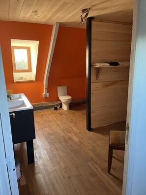 Ein Zimmer mit Holzboden, einer weißen Toilette, einem Fenster mit Aussicht und einem Waschbecken.