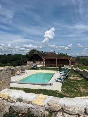 Ein Poolbereich mit Liegestühlen, einer Steinmauer und einem Gebäude mit einem Reetdach im Hintergrund.