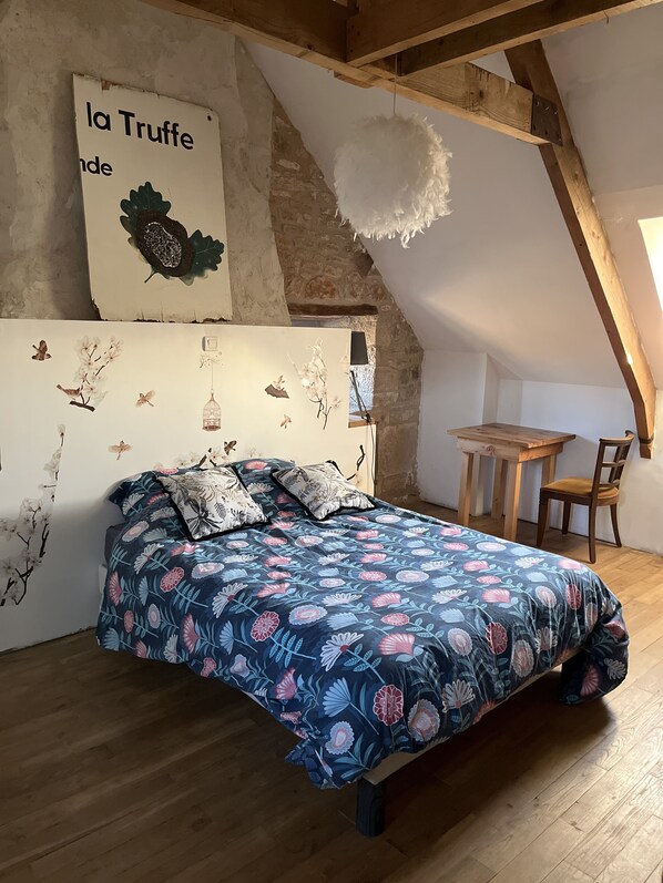 Ein Schlafzimmer mit Holzboden, einem Bett mit Blumenmuster-Bettwäsche, einem Holztisch und einem Stuhl.