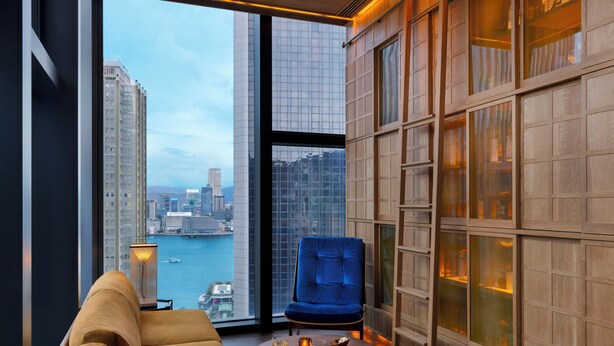 A modern room with a large window, a blue chair, a sofa, and a small table with glasses. - AKI Hotel Hong Kong - MGallery Collection (Hong Kong)