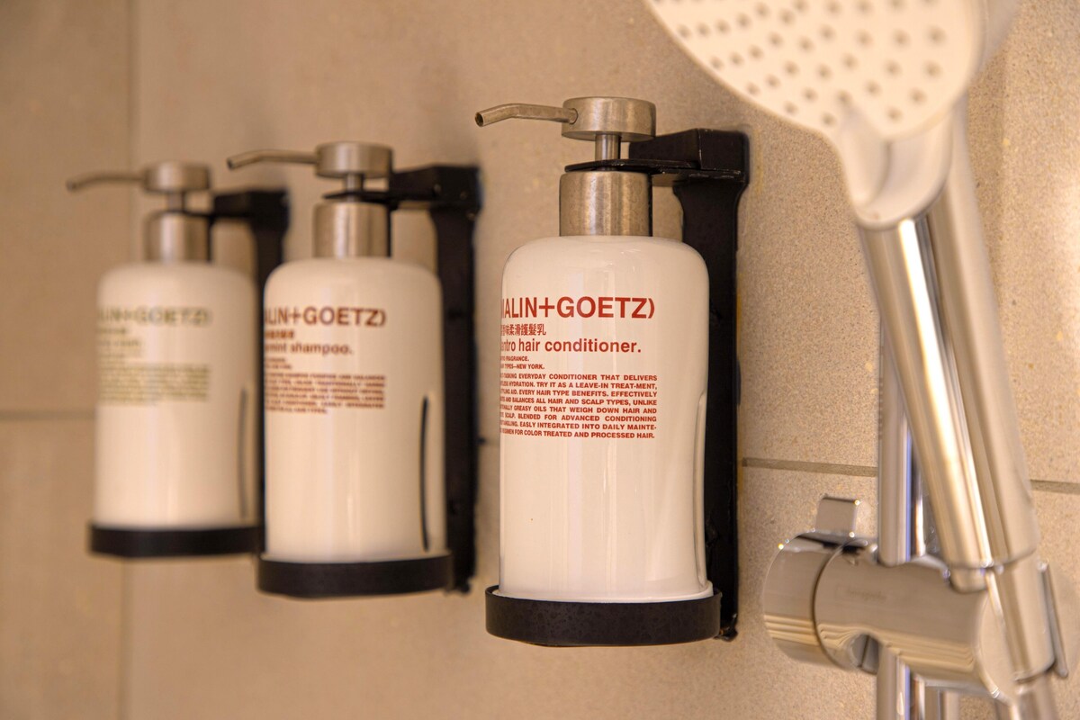 Une salle de bain avec trois flacons d’après-shampoing et un pommeau de douche.