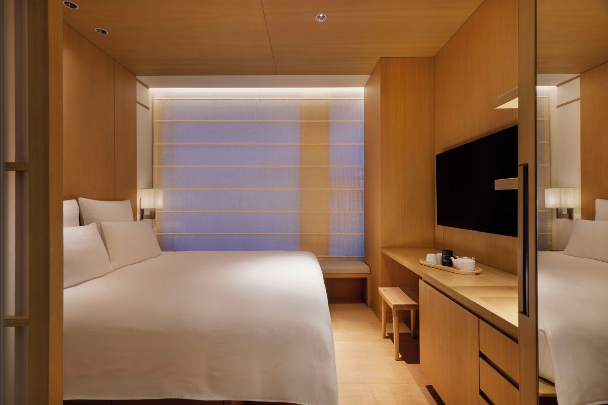 Une chambre d’hôtel moderne dotée d’un grand lit, d’un bureau avec un téléviseur à écran plat et d’un coin salon offrant une vue à travers une cloison en verre dépoli.