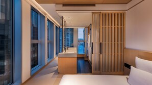 A modern hotel room with a large bed, a bathroom with a sink, and a view of the cityscape through large windows. - AKI Hotel Hong Kong - MGallery Collection (Hong Kong)