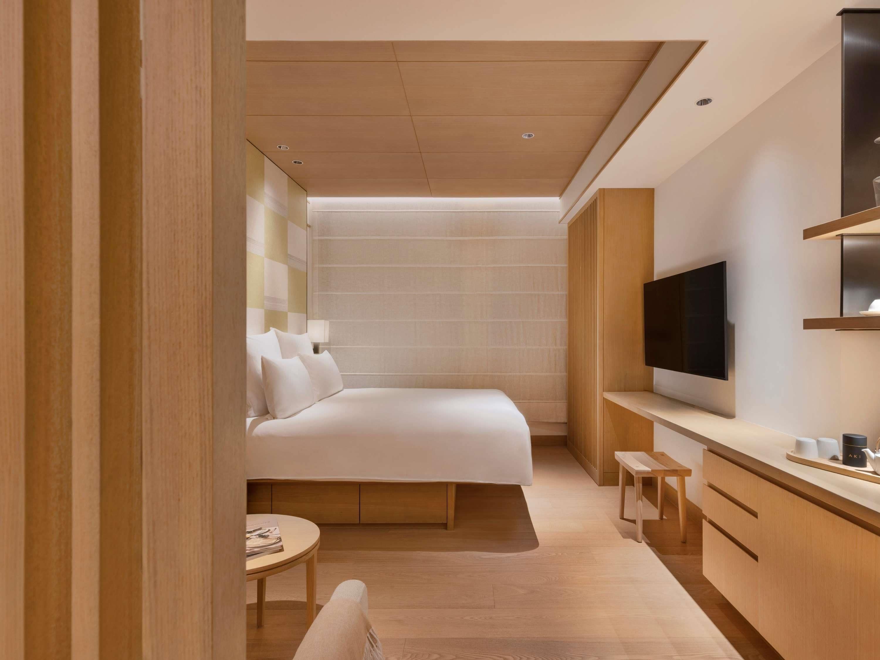 Ein modernes Hotelzimmer mit einem Bett, einem Fernseher, einem kleinen Tisch und einer Bank.