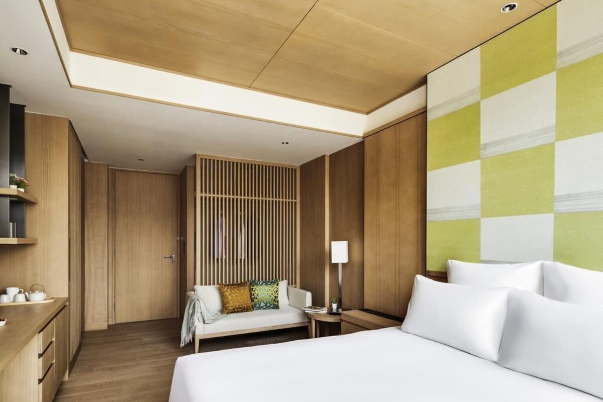 Une chambre d’hôtel moderne équipée d’un lit, d’une table de chevet, d’une lampe et d’un coin salon avec un canapé et des coussins.