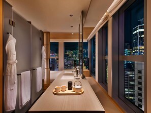 Une chambre d’hôtel moderne, de forme longue et étroite, avec vue sur le paysage urbain illuminé la nuit, et un service à thé posé sur le comptoir.