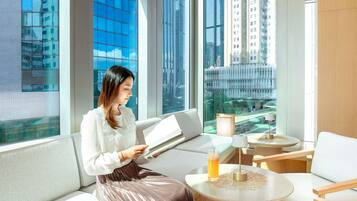 Una habitación de hotel moderna con ventanas amplias, un sofá, una mesa redonda y una lámpara.