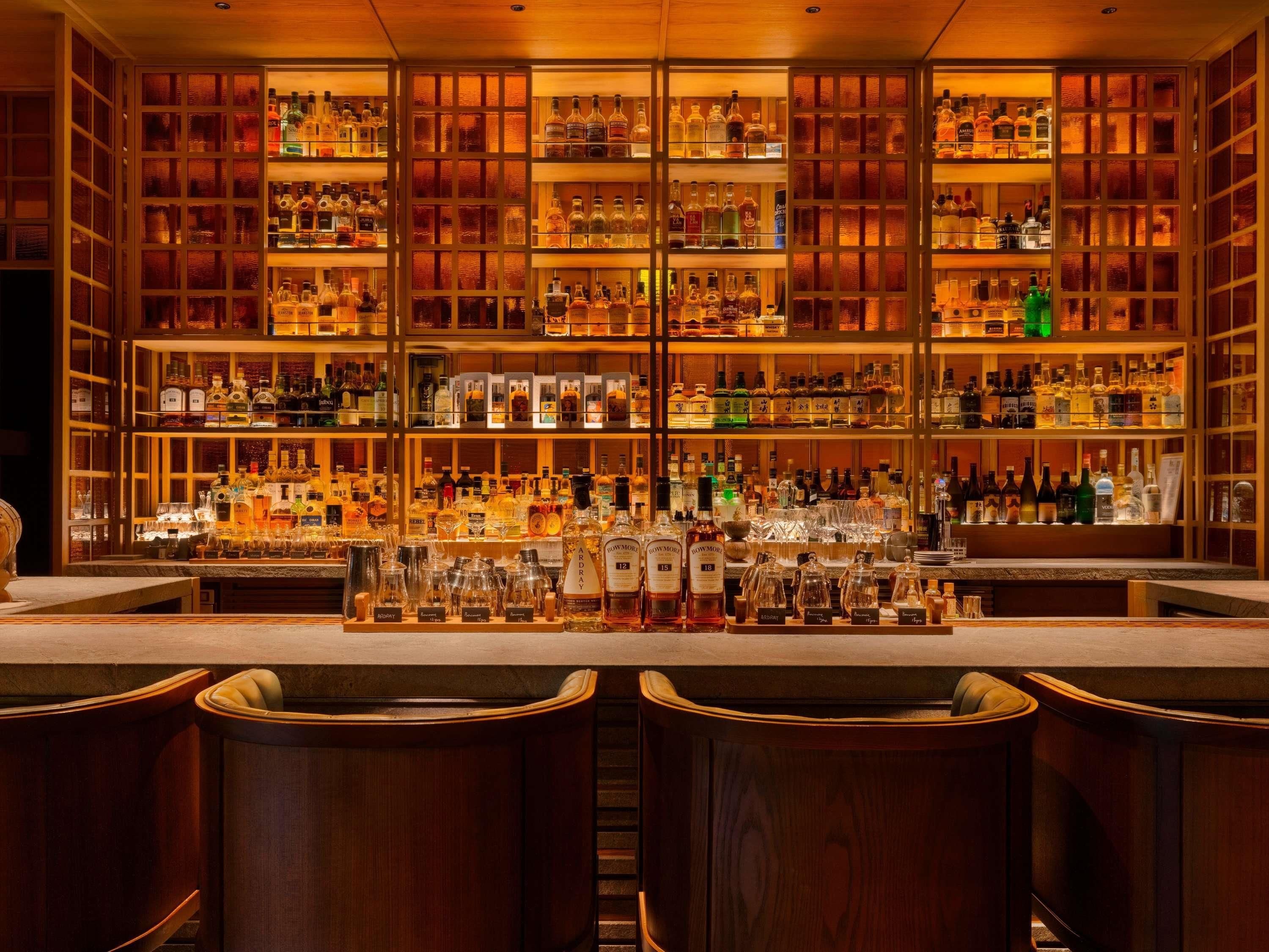 A bar with multiple shelves of liquor bottles and glasses, wooden bar counter, and bar stools.