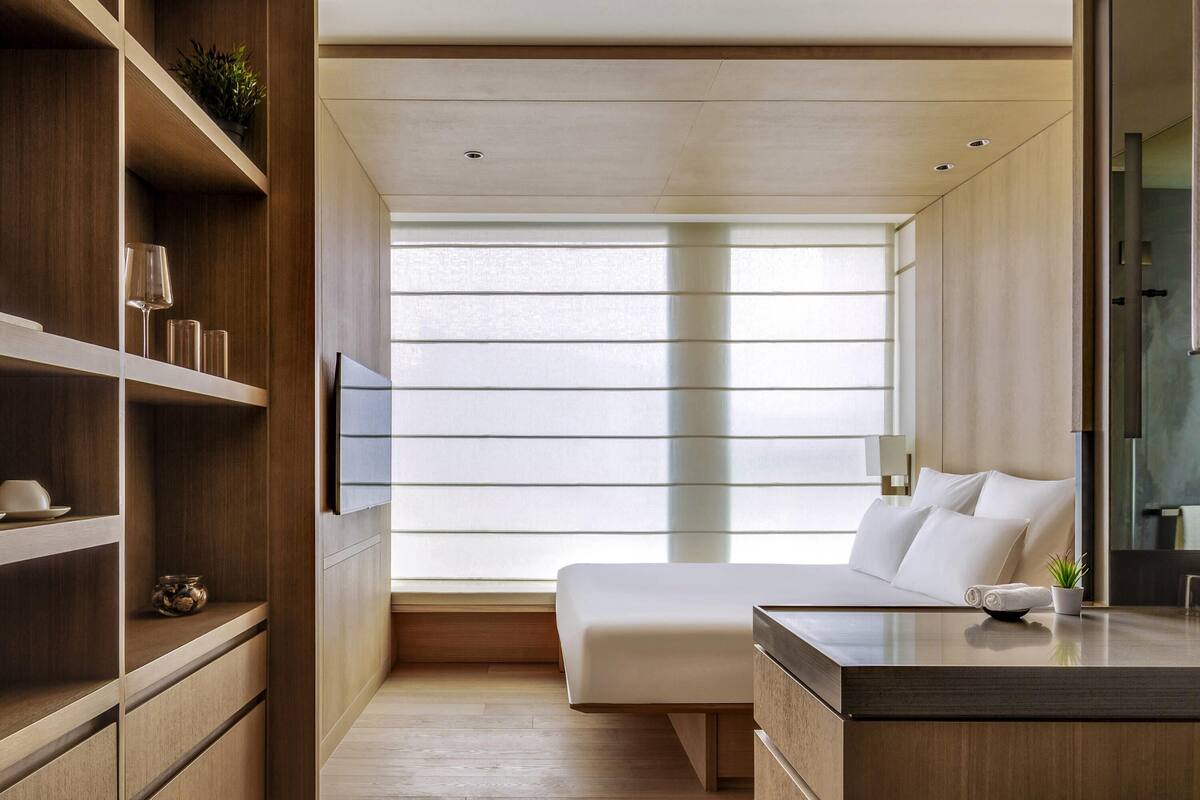 A modern bedroom with a large window, built-in shelving, and a bedside table.