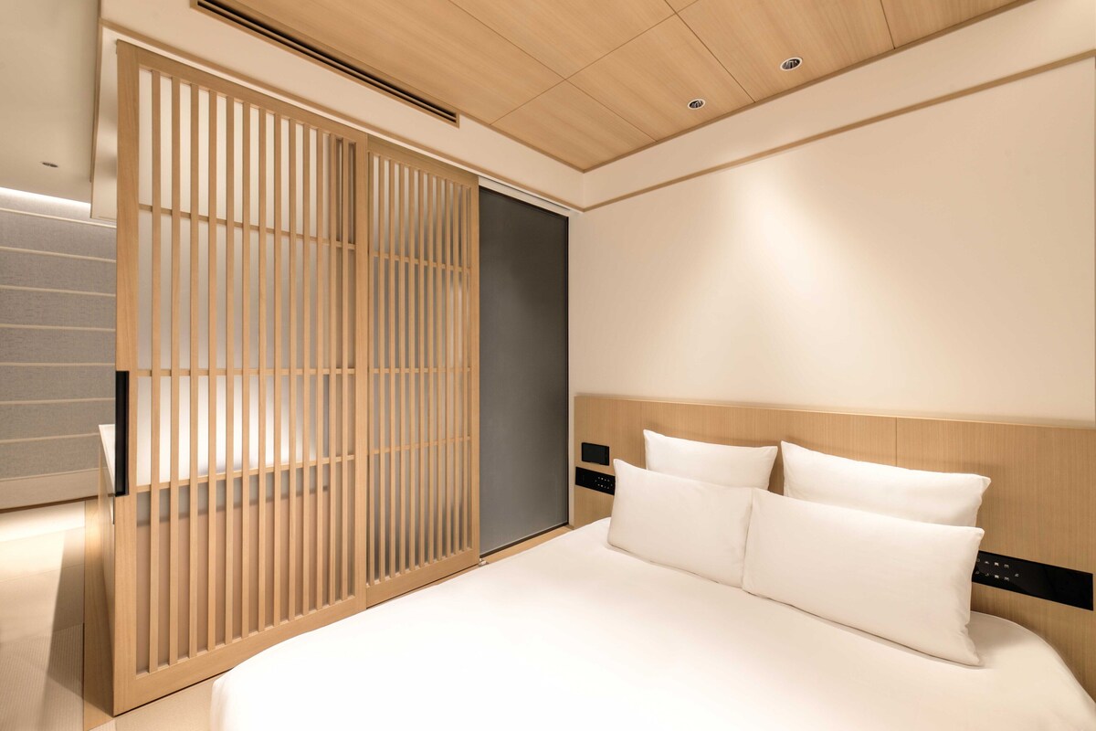 Une chambre d’hôtel moderne dotée d’un grand lit, d’une porte coulissante en bois et d’un design minimaliste.