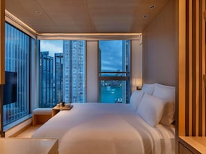 A modern hotel room with a large bed, a TV, a bedside table, and a view of tall buildings and a body of water. - AKI Hotel Hong Kong - MGallery Collection (Hong Kong)