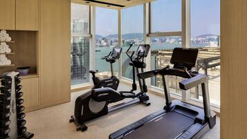A modern gym with cardio equipment, a weight bench, and a view of a cityscape through large windows.