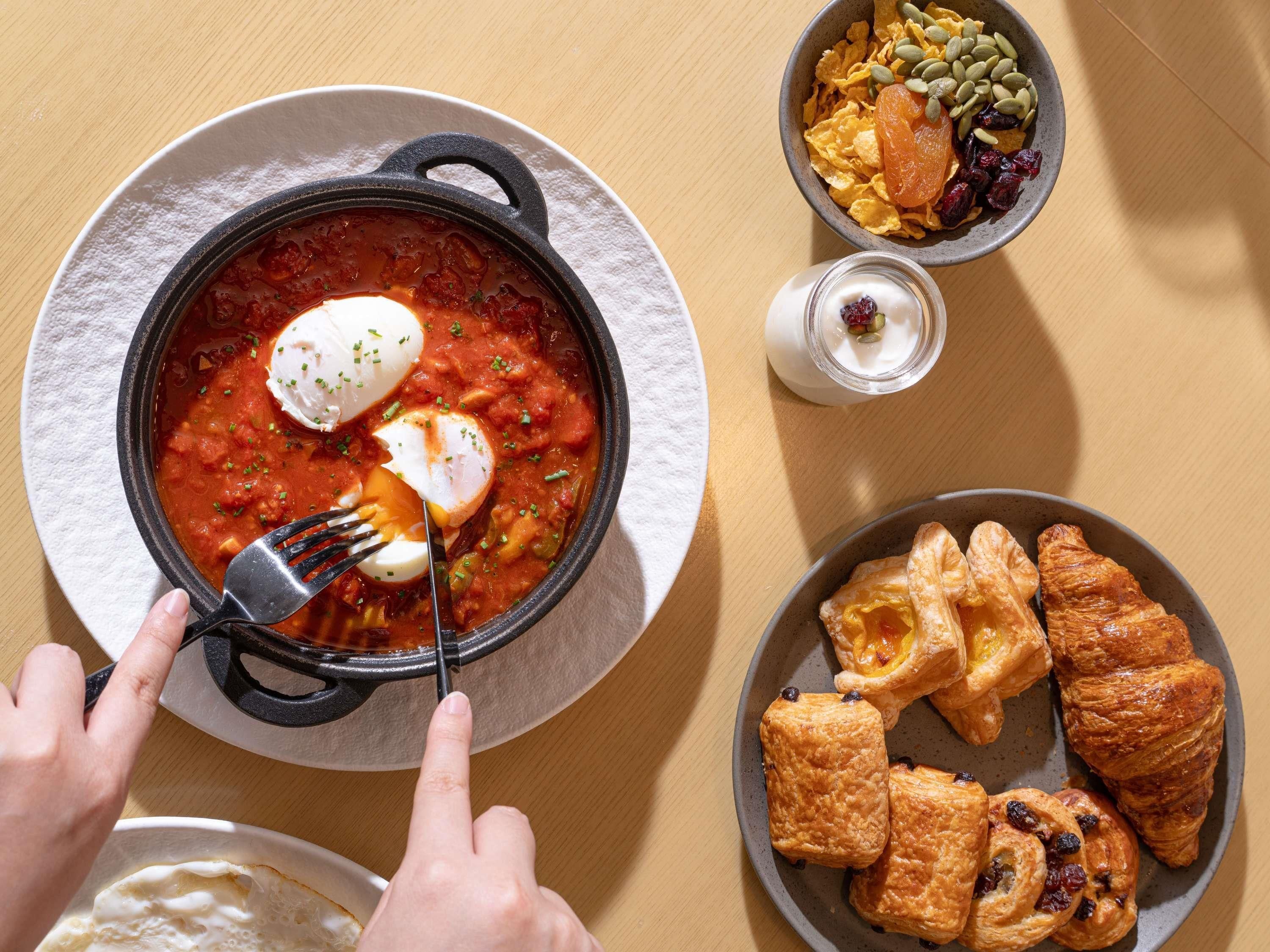A meal with a bowl of soup, a plate of pastries, and a bowl of cereal with fruits and nuts.