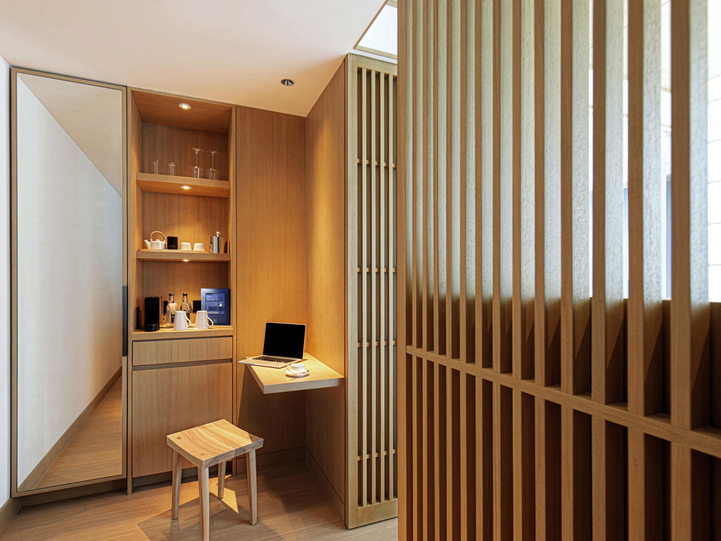 A compact, modern room with a wooden desk, a laptop, and a small wooden stool.