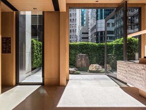 Un hall d’hôtel moderne avec un comptoir d’accueil, un ascenseur en verre et une vue sur le paysage urbain.