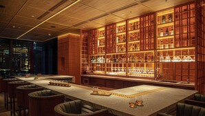 A bar area with a long counter, multiple stools, and shelves stocked with bottles and glasses. - AKI Hotel Hong Kong - MGallery Collection (Hong Kong)