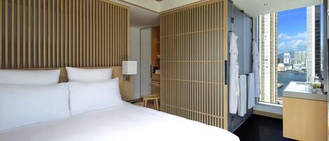 A hotel room with a large bed, a wooden partition, a small table, a chair, a desk with a mirror, and a view of a cityscape.
