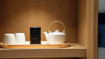 Un estante de madera con una tetera blanca, una taza negra con la etiqueta "AKI" y dos tazas blancas.