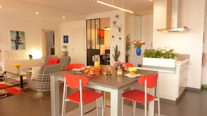 A modern living room with a dining area, featuring a sofa, red chairs, a coffee table, and a breakfast setup with pastries and drinks. - Vannes, 4-star luxury flat with car park (Vannes)
