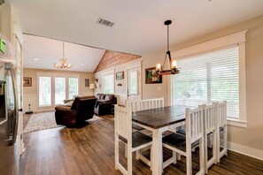 A spacious living room with a fireplace, a dining area with a wooden table and chairs, and large windows with blinds. - Okatoma River Cabin/ Convenient Location (Collins)