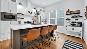 Une cuisine moderne avec des meubles blancs, un grand îlot central doté de tabourets, un micro-ondes encastré et un réfrigérateur.