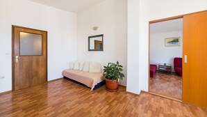 A room with a wooden floor, a sofa, a potted plant, a mirror, and a door leading to another room. - Stunning 3-bedroom Apartment in Gradac (Gradac)