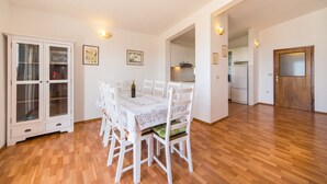 A spacious dining area with a white table and chairs, a cabinet with glass doors, and a kitchen in the background. - Stunning 3-bedroom Apartment in Gradac (Gradac)