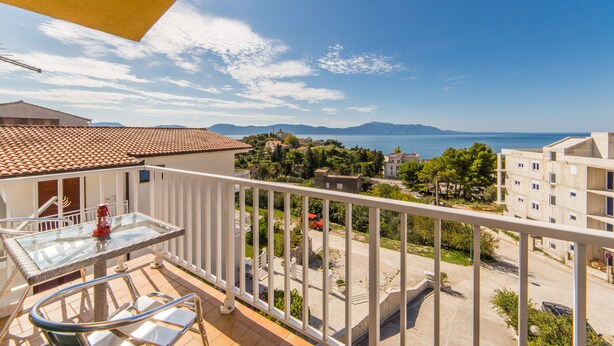 A balcony with a clear view of the sea and distant mountains, a tiled roof, and a glass table with chairs. - Stunning 3-bedroom Apartment in Gradac (Gradac)
