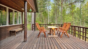 Eine Holzterrasse mit Tisch und Stühlen, umgeben von einem Holgitter, mit Blick auf ein bewaldetes Gebiet.