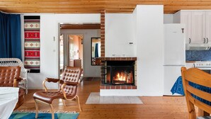 Ein gemütliches Wohnzimmer mit Kamin, Ledersesseln, einer Essecke und einer Küche mit weißen Schränken.