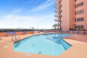 A swimming pool with lounge chairs and a building with balconies.