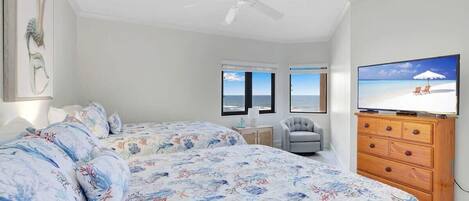 A bedroom with a bed, a television, a ceiling fan, and a view of the ocean through a window.