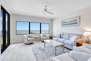 A modern living room with a large window, a ceiling fan, a sofa, a coffee table, and a painting on the wall.