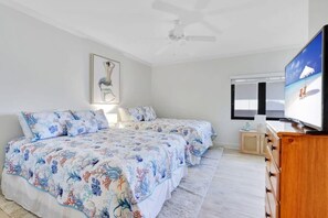 Ein Schlafzimmer mit zwei Betten, einem Deckenventilator, einem Fernseher und einem gerahmten Bild an der Wand.