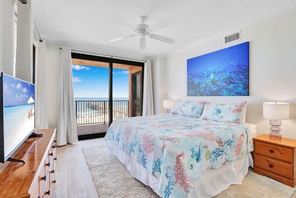 Ein Schlafzimmer mit Bett, Fernseher, Deckenventilator, einem Gemälde und einem Balkon mit Blick.