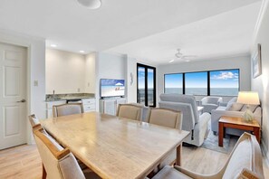 A modern living room with a dining table, sofas, and a television.
