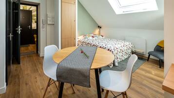 A compact room with a bed, a dining table with chairs, a small table, and a skylight.