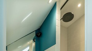Un bagno moderno con un mobile lavabo bianco, uno specchio, una doccia con un tubo nero e un tappetino da bagno giallo.