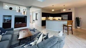 Un salon moderne avec un canapé, une table basse et un téléviseur. Il y a également un coin cuisine équipé d’un réfrigérateur et d’une table à manger.