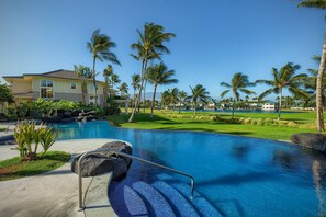 Una piscina con borde de piedra, palmeras y un campo de golf al fondo.