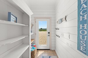 Um corredor estreito com paredes brancas, uma porta que dá para a praia, e uma placa com a inscrição 'BEACH HOUSE'.