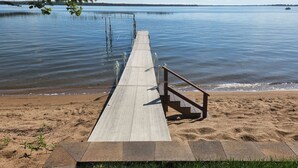 A wooden pier extending into calm water, with a sandy beach and a grassy area at the end. - Beautiful, family friendly Lake home w/sunroom and 100ft of sandy beach! (Henning)