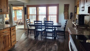 A spacious kitchen with wooden cabinets, a dining table with chairs, and large windows offering a view of the outdoors. - Beautiful, family friendly Lake home w/sunroom and 100ft of sandy beach! (Henning)