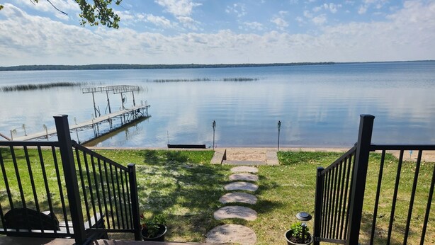 A wooden deck with a view of a calm lake and a dock. - Beautiful, family friendly Lake home w/sunroom and 100ft of sandy beach! (Henning)