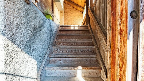 A wooden staircase leading to a room with a sloped ceiling and a window.