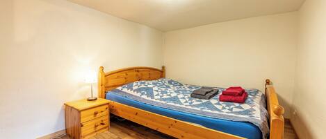 A small, single-bed room with a wooden headboard, a bedside table with a lamp, and a wooden floor.
