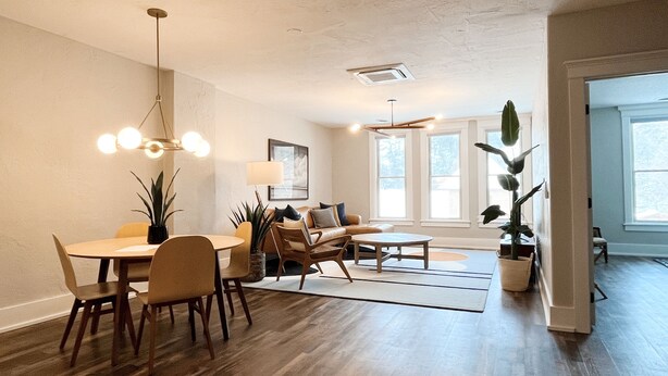 A spacious living area with a dining table, chairs, and a sofa. There are large windows providing natural light and a view of the outdoors. - Historic & Modern! Walk to Restaurants, Moccasin Springs + Huge Suite w/ Kitchen (Hot Springs)